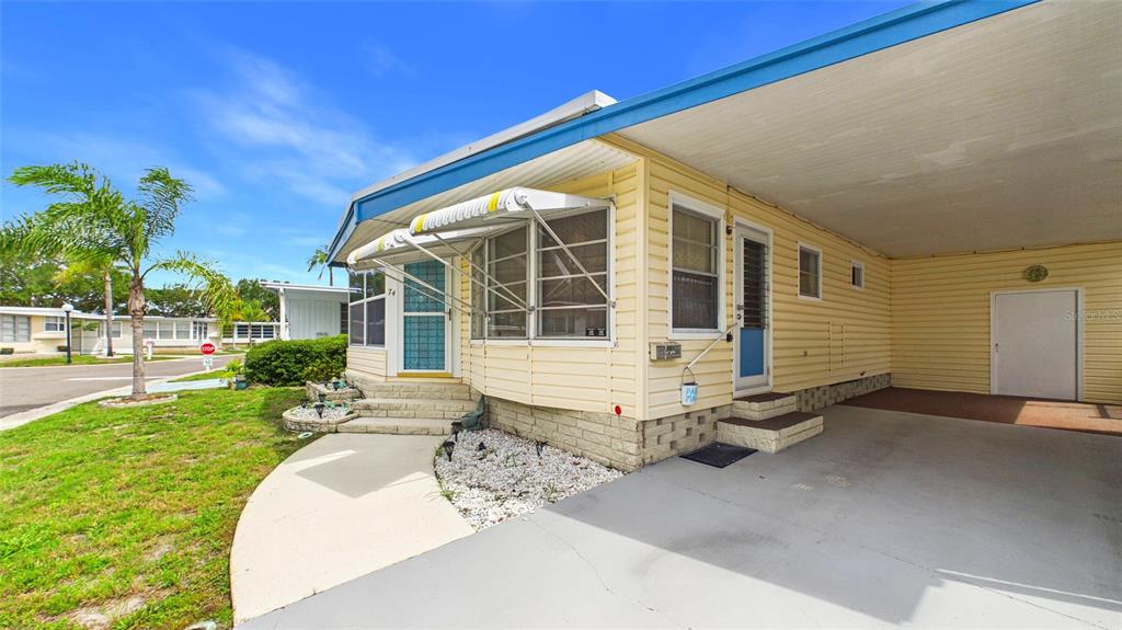 A yellow mobile home with a carport, a concrete driveway, and a small front garden — 7901 40TH AVENUE N UNIT 74, ST PETERSBURG, FL