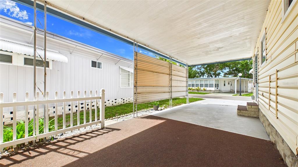 A covered carport with a brown floor mat, white fence, and beige siding — 7901 40TH AVENUE N UNIT 74, ST PETERSBURG, FL