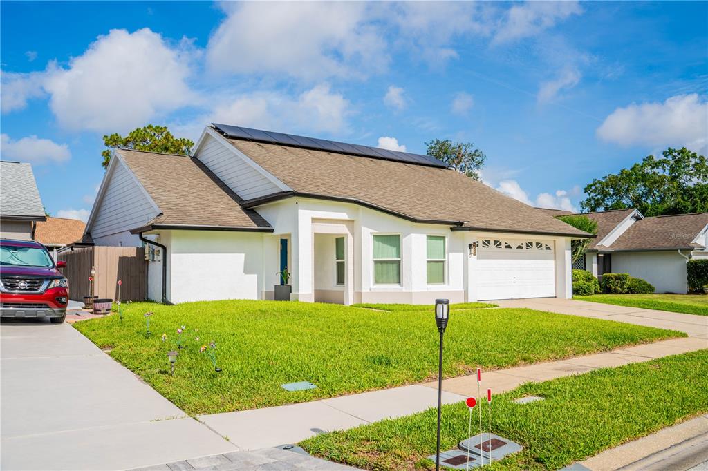 A single-story house with a white stucco exterior, a brown shingled roof, and solar panels — 623 HOLBROOK CIRCLE, LAKE MARY, FL