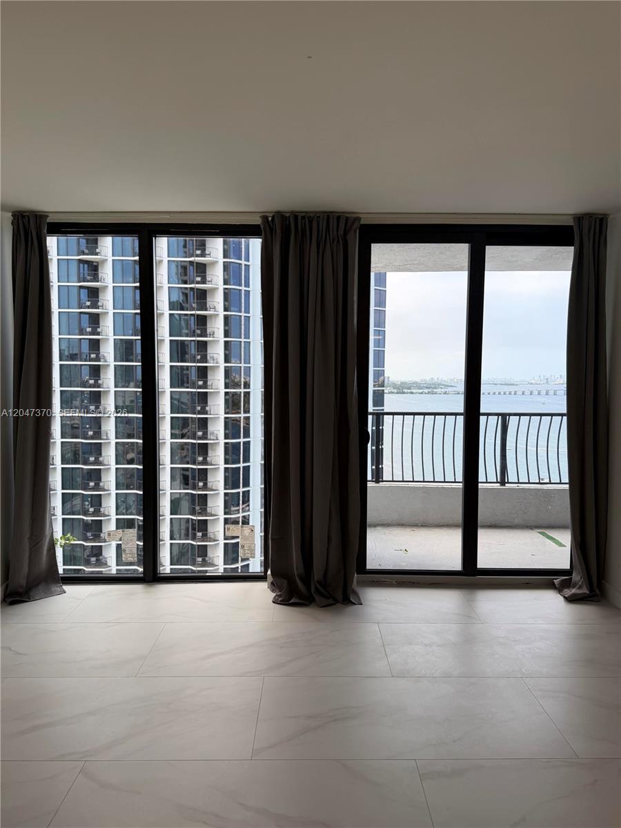A room with light-colored tile flooring features floor-to-ceiling windows overlooking a balcony and water — 555 NE 15th St # 23D, Miami FL 33132, MIAMI, FL