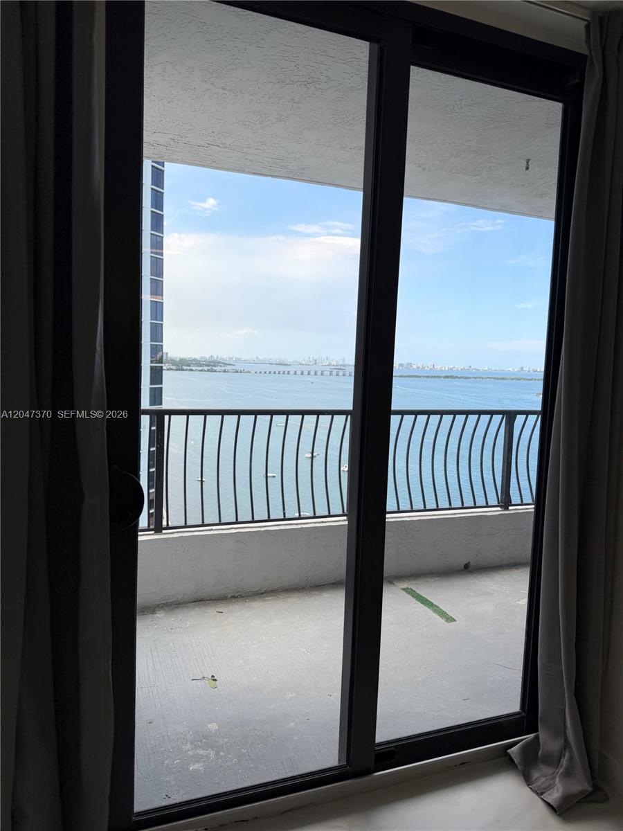 A sliding glass door opens onto a balcony overlooking a bay and city skyline — 555 NE 15th St # 23D, Miami FL 33132, MIAMI, FL