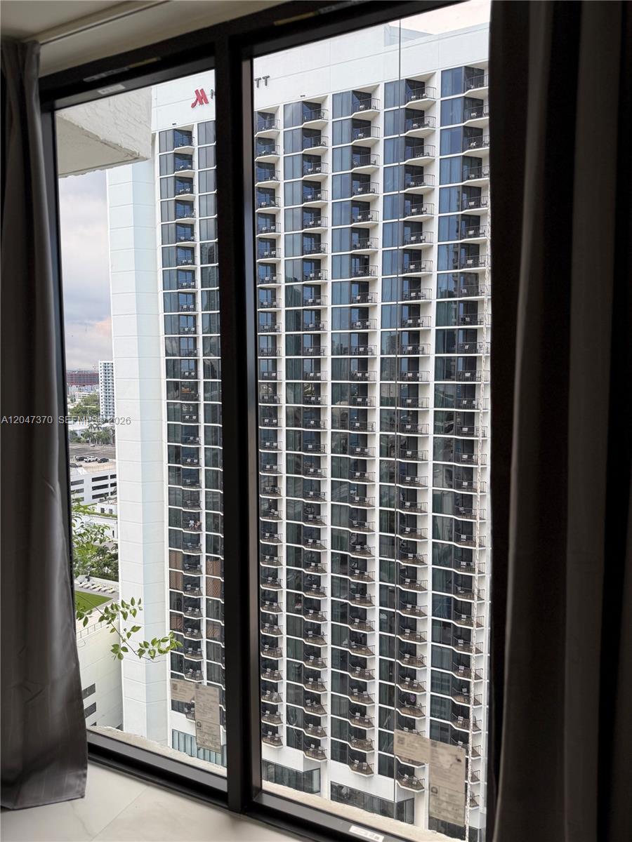 A view through a window shows a tall, modern hotel building with numerous balconies — 555 NE 15th St # 23D, Miami FL 33132, MIAMI, FL
