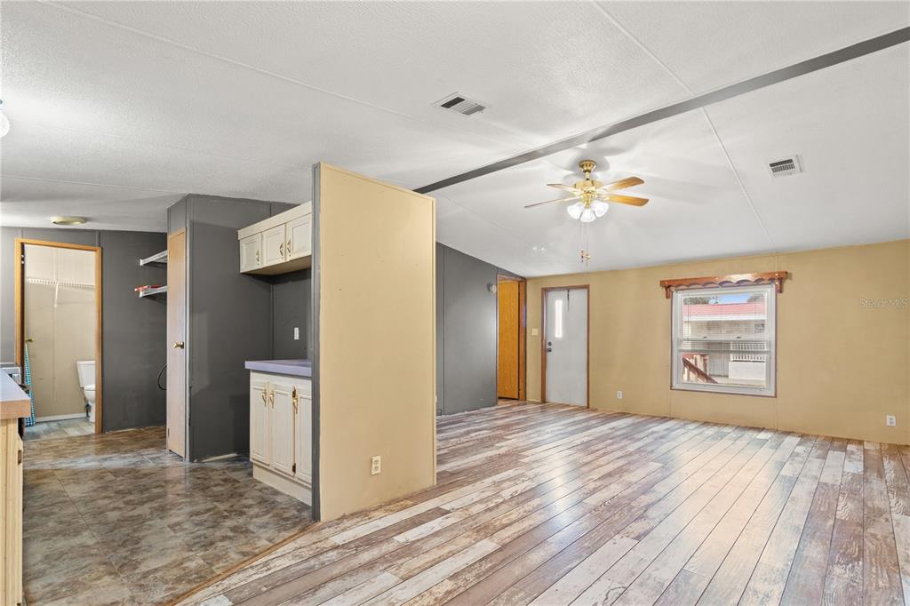 An interior view shows a living area with wood-look flooring, a ceiling fan, and kitchen cabinets — 1371 NW 12TH LANE, LAKE PANASOFFKEE, FL