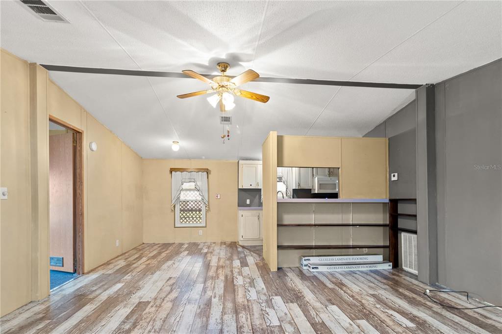 A living room features wood-look laminate flooring, a ceiling fan, and a partial kitchen wall — 1371 NW 12TH LANE, LAKE PANASOFFKEE, FL