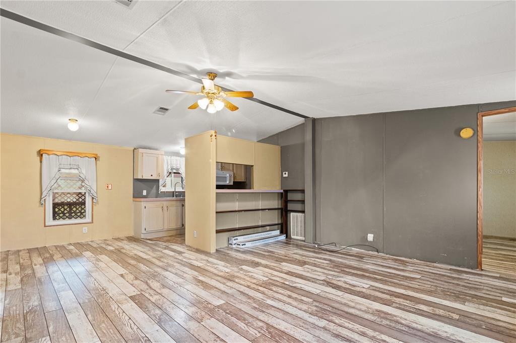 A living room with wood-look flooring, a ceiling fan, and an open kitchen area — 1371 NW 12TH LANE, LAKE PANASOFFKEE, FL
