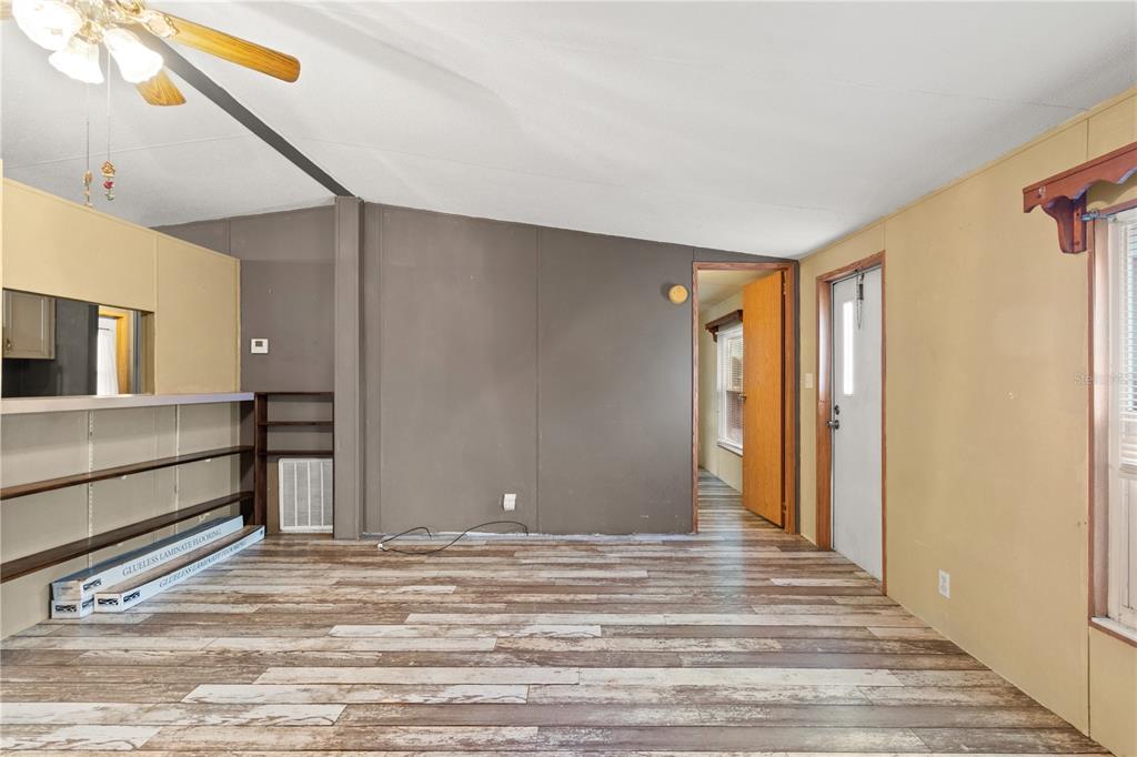 A living room with wood-look laminate flooring, a dark accent wall, and a ceiling fan — 1371 NW 12TH LANE, LAKE PANASOFFKEE, FL