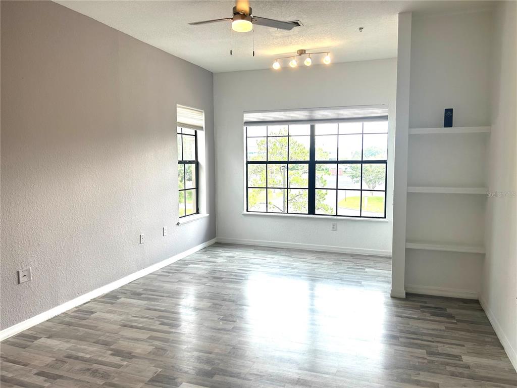 An empty room features gray walls, wood-look flooring, a ceiling fan, and built-in shelving — 6137 METROWEST BOULEVARD UNIT 307, ORLANDO, FL