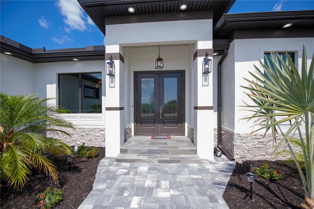 The exterior of a modern home features a double front door, stone siding, and landscaping — 11 PINEHURST COURT, ROTONDA WEST, FL