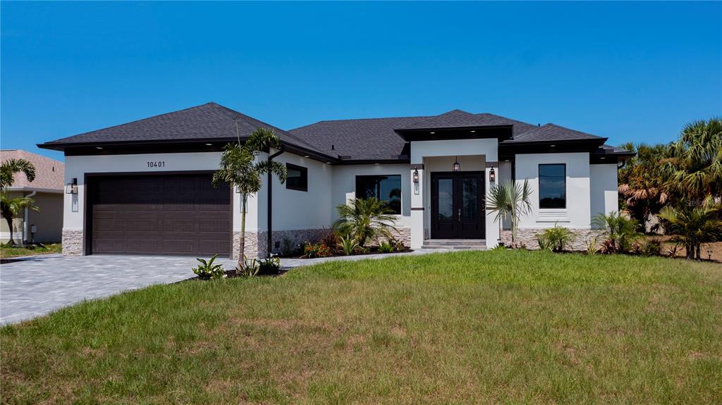 A modern single-story house with a dark garage door, stone accents, and a paved driveway — 11 PINEHURST COURT, ROTONDA WEST, FL