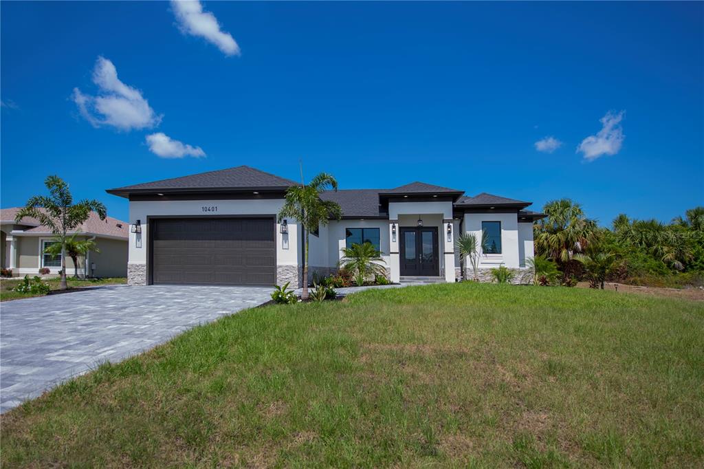 A modern single-story house with a two-car garage, stone accents, and a paved driveway — 11 PINEHURST COURT, ROTONDA WEST, FL