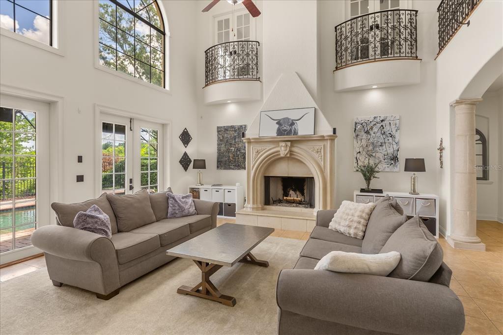 A high-ceilinged living room features a stone fireplace, two gray sofas, and indoor balconies — 1244 E LAKE COLONY DRIVE, MAITLAND, FL