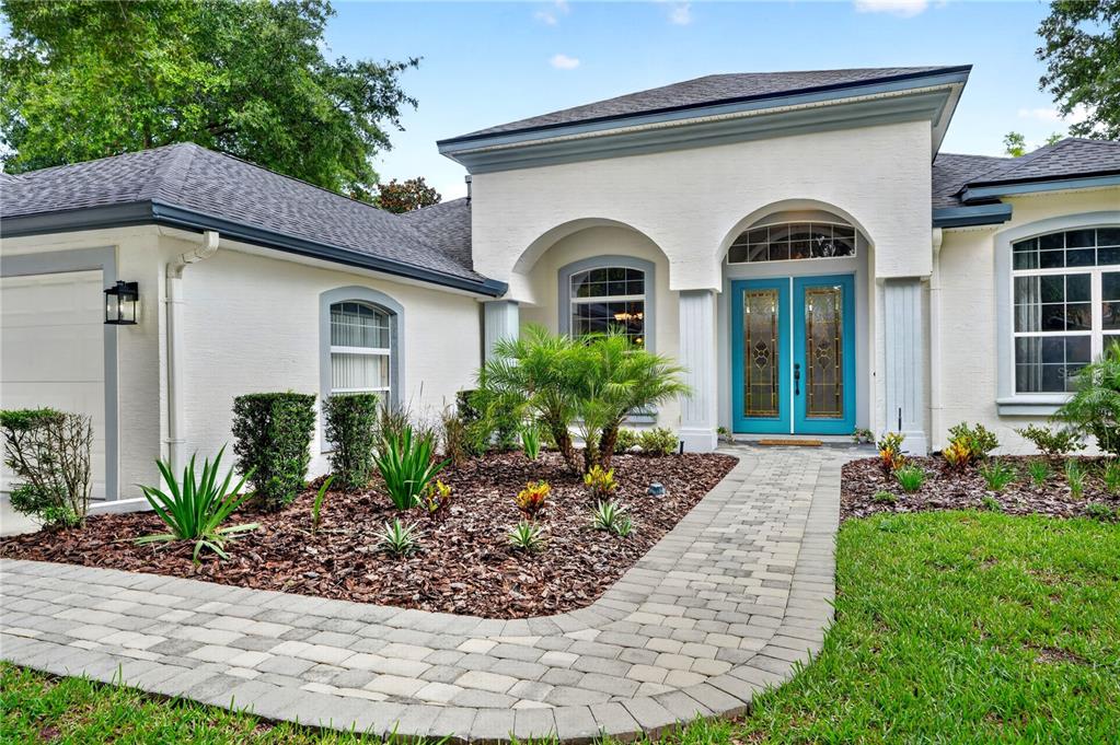 A white house exterior features a paved walkway leading to a bright blue double front door — 1435 DOLPH CIRCLE, ORMOND BEACH, FL