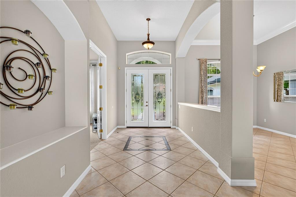 A tiled entryway features double glass-paneled front doors, a decorative wall sculpture, and arched openings — 1435 DOLPH CIRCLE, ORMOND BEACH, FL