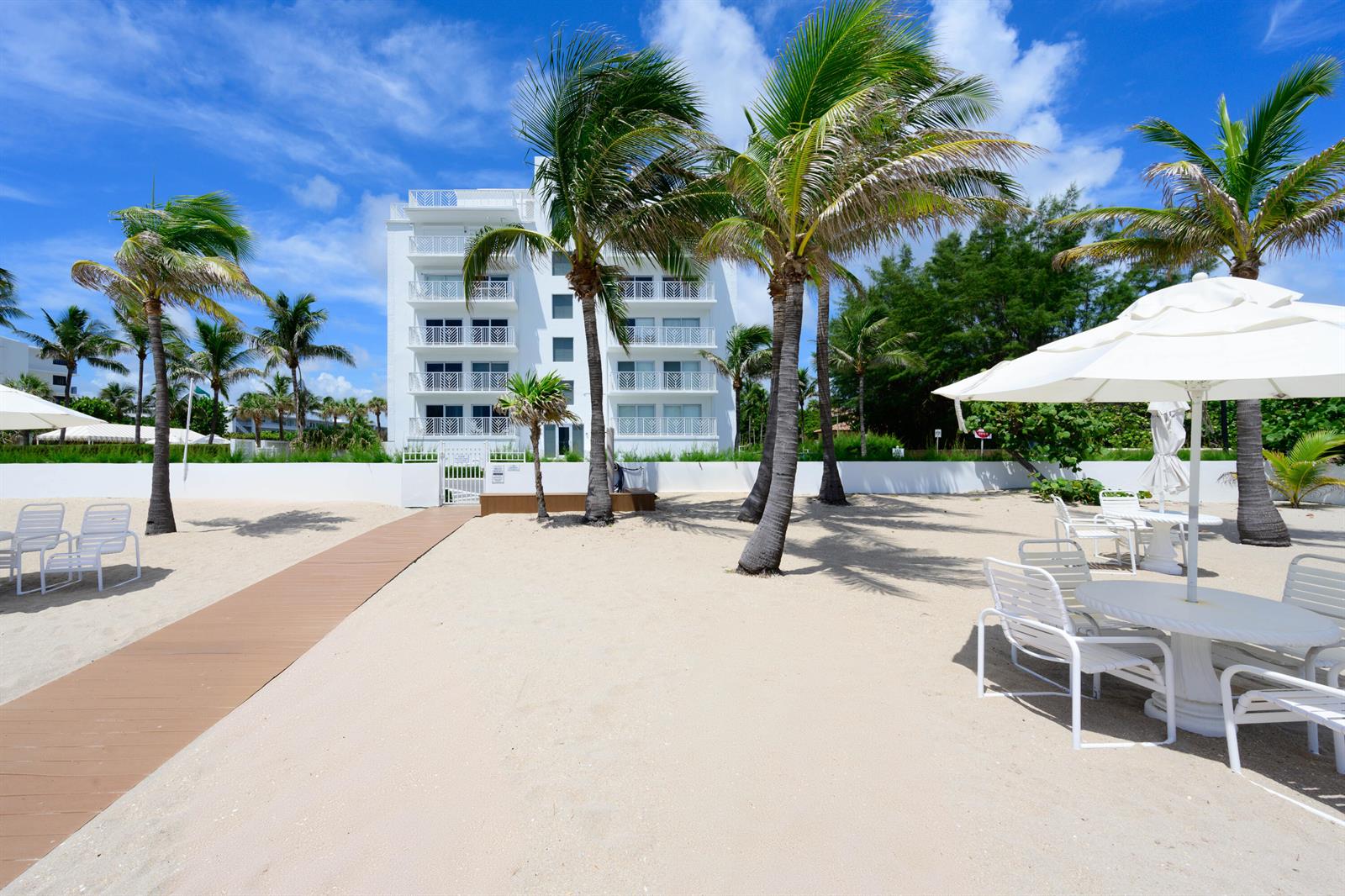 A white multi-story building stands behind a sandy beach with palm trees and patio furniture — 170 N Ocean Boulevard # 303, Palm Beach FL 33480, PALM BEACH, FL