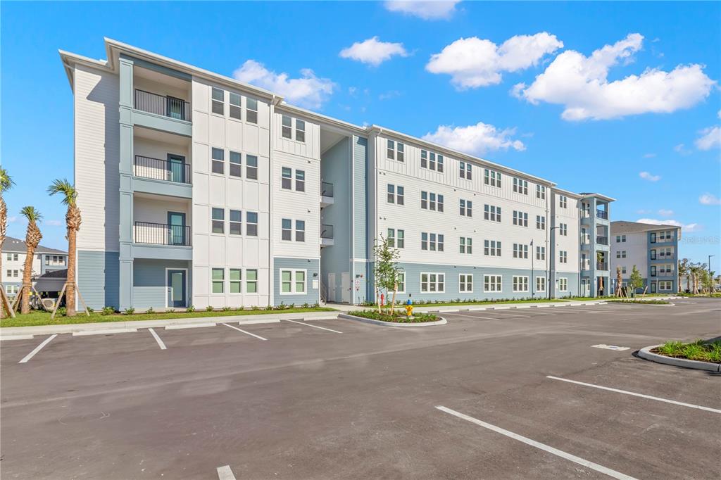 A multi-story apartment building with a parking lot in the foreground under a blue sky — 9720 BEAMING ROAD UNIT C1.2, VENICE, FL