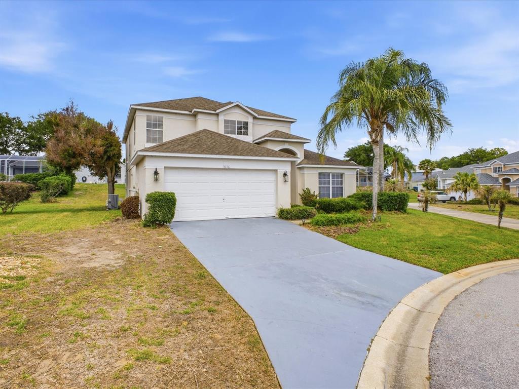 A two-story suburban house with a white garage, gray driveway, and a palm tree — 1656 DUNES COURT, HAINES CITY, FL