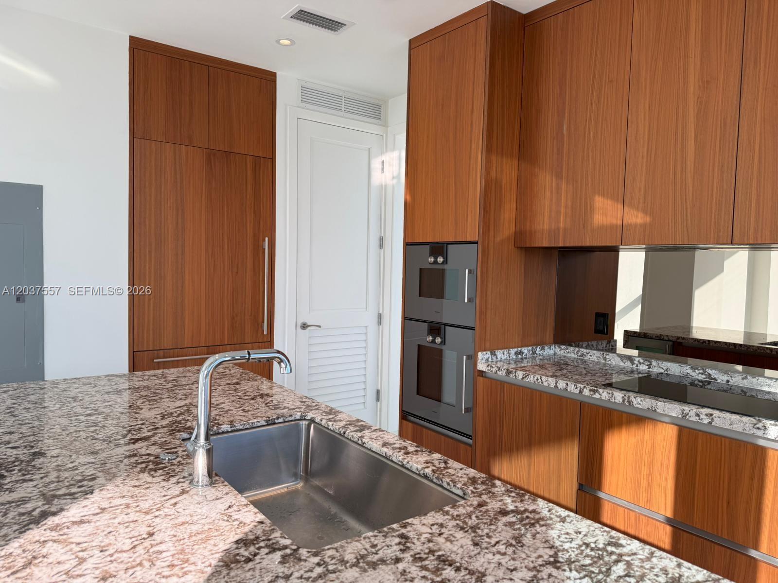 A modern kitchen features wood cabinetry, granite countertops, a stainless steel sink, and built-in ovens — 175 SE 25th Rd # 903, Miami FL 33129, MIAMI, FL