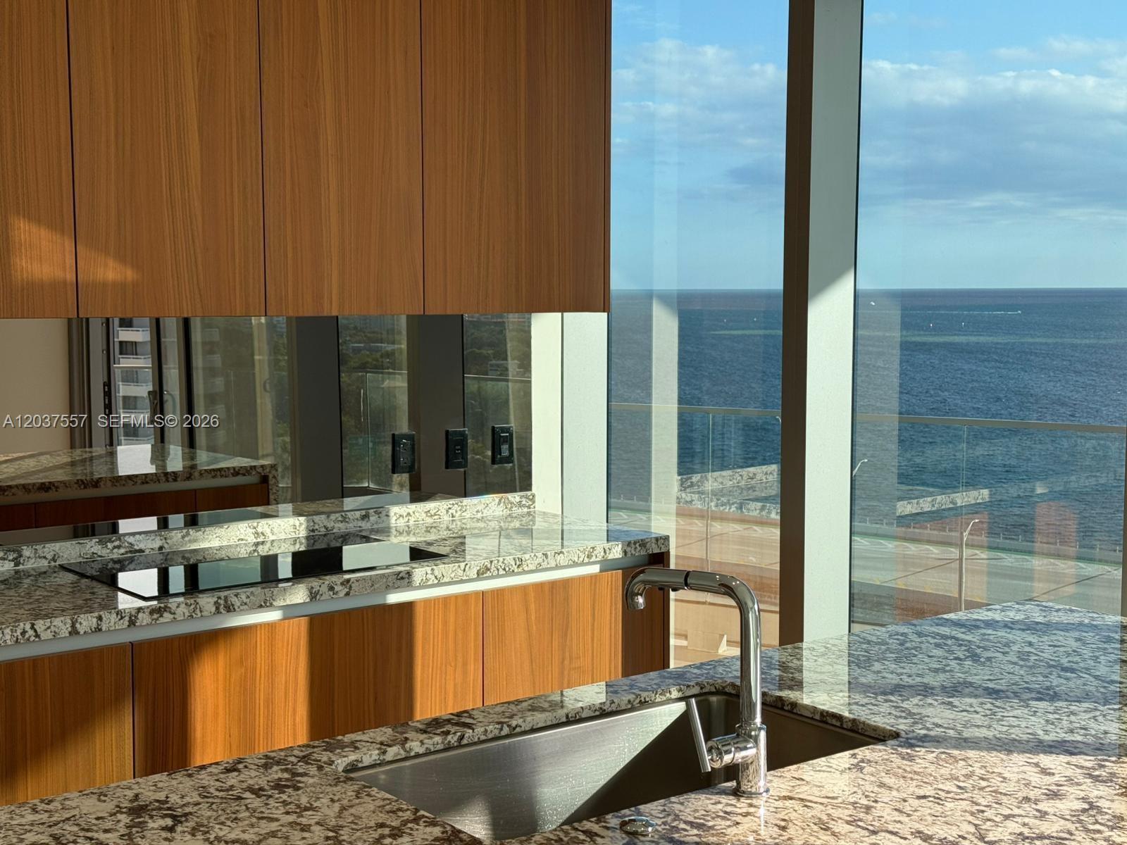 A kitchen features wood cabinets, granite countertops, and floor-to-ceiling windows overlooking the ocean — 175 SE 25th Rd # 903, Miami FL 33129, MIAMI, FL