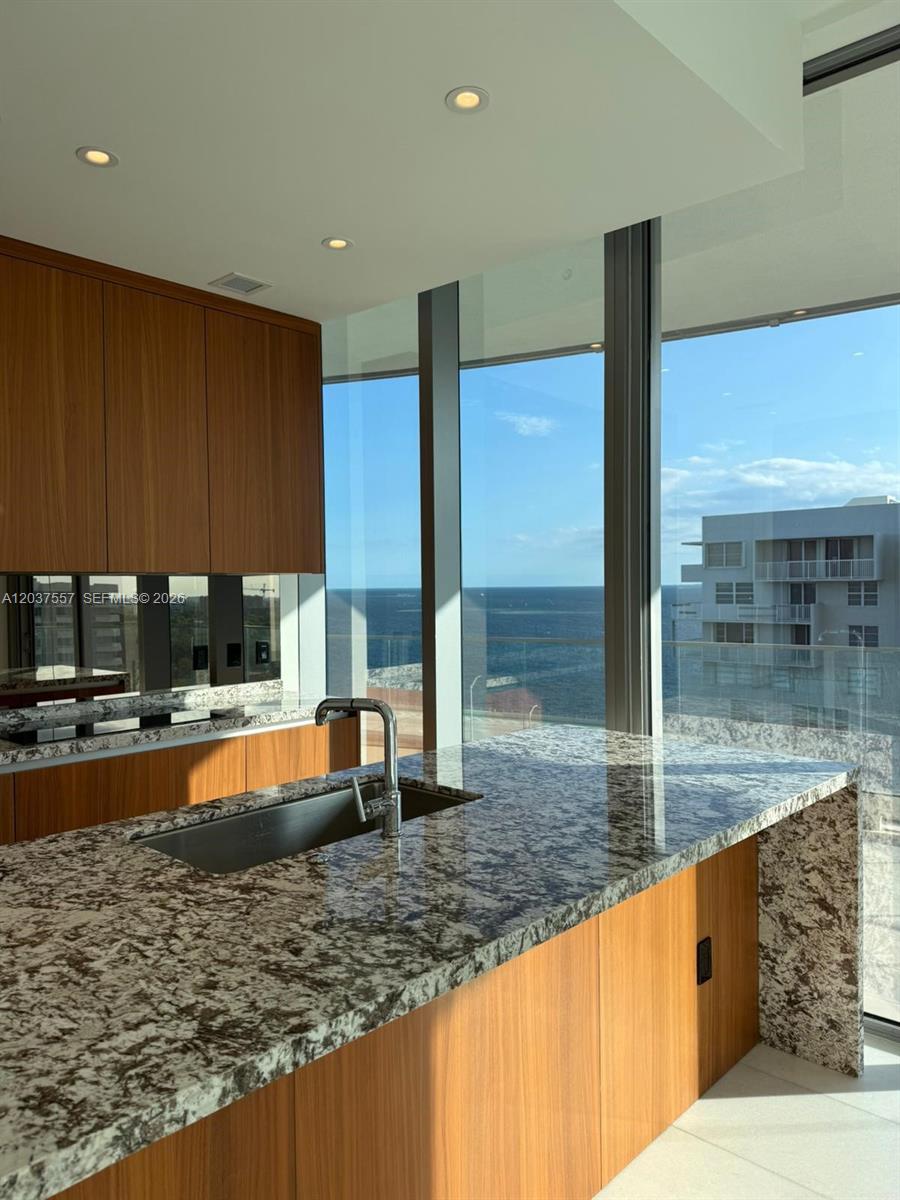 A modern kitchen features wood cabinets, granite countertops, and floor-to-ceiling windows overlooking the ocean — 175 SE 25th Rd # 903, Miami FL 33129, MIAMI, FL