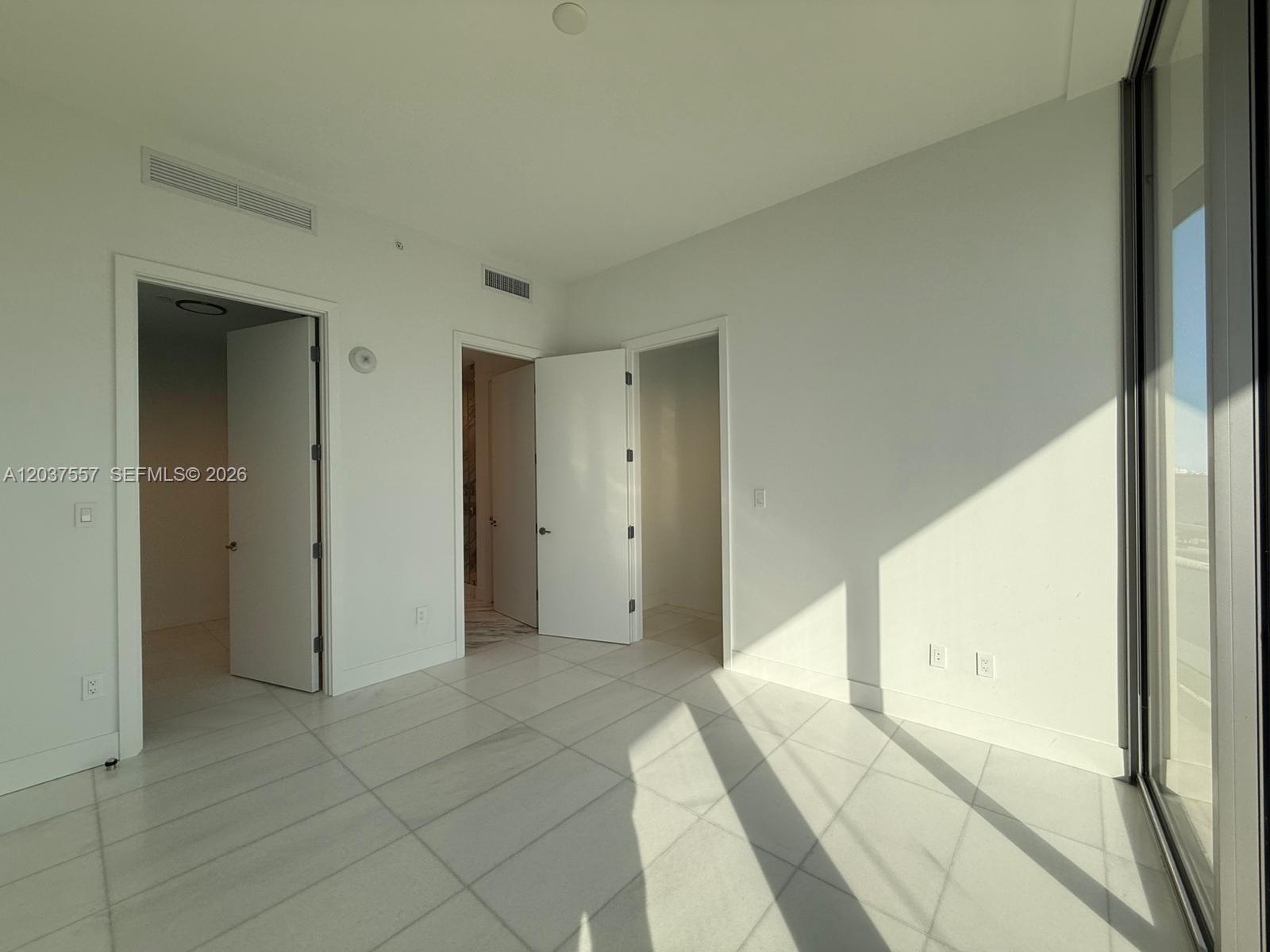 A bright, minimalist room features white tile flooring, two open doorways, and floor-to-ceiling windows — 175 SE 25th Rd # 903, Miami FL 33129, MIAMI, FL