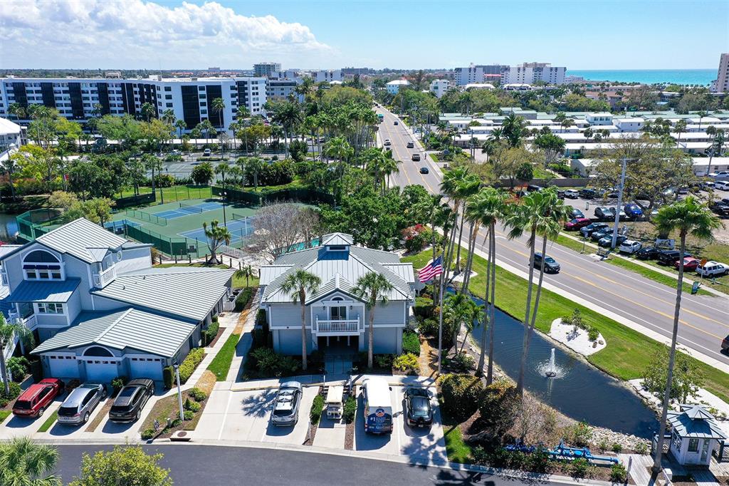 An aerial view shows a coastal neighborhood with houses, tennis courts, and a nearby road — 1200 SIESTA BAYSIDE DRIVE UNIT 1200G, SARASOTA, FL