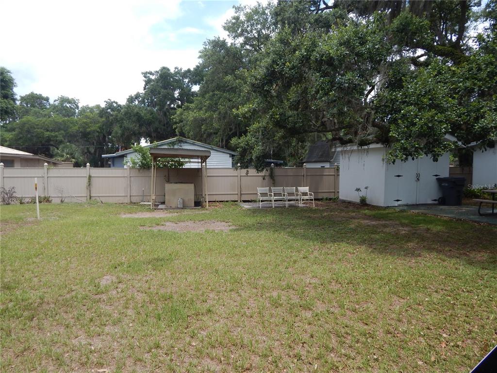 A grassy backyard features a tan fence, a small covered structure, and a white shed — 21 ANCHOR INN ROAD, LAKE WALES, FL