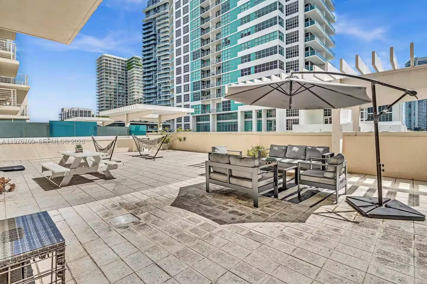 A spacious rooftop terrace features outdoor furniture, a large umbrella, and hammocks between tall buildings — 3250 NE 1st Ave # 501, Miami FL 33137, MIAMI, FL
