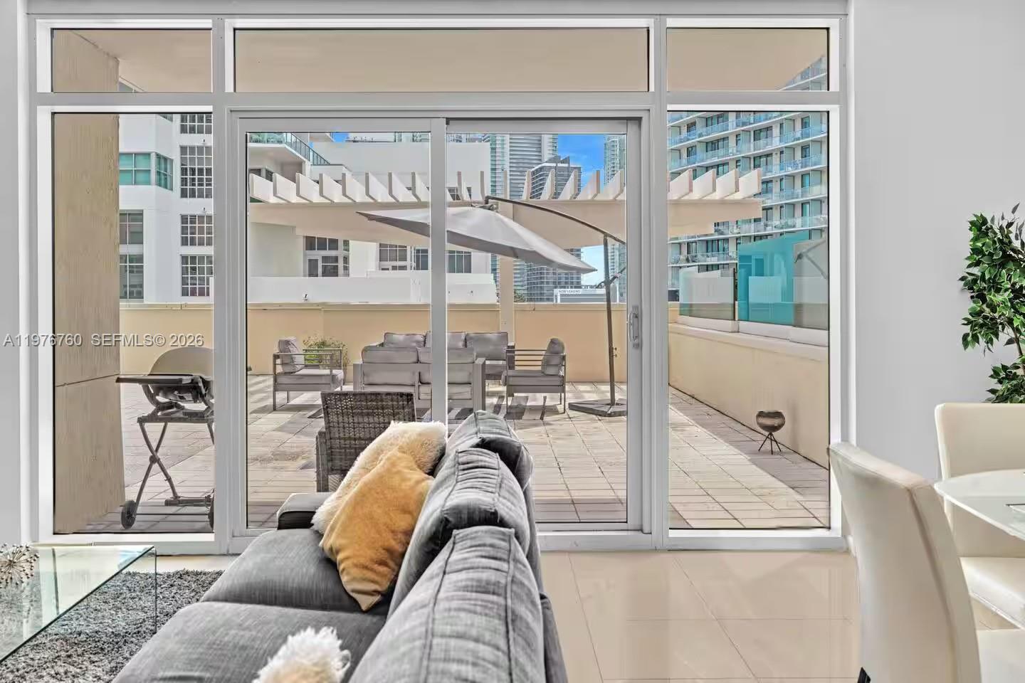 A living room with a gray sofa looks out through sliding glass doors onto a terrace — 3250 NE 1st Ave # 501, Miami FL 33137, MIAMI, FL