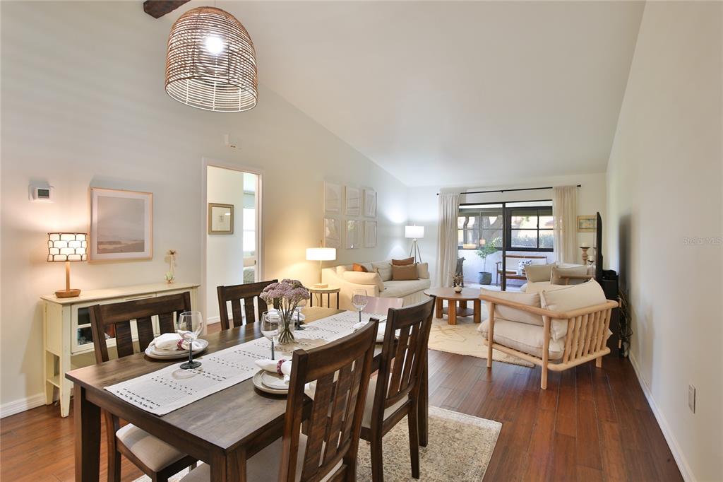 A dining area with a wooden table leads into a living room with hardwood floors — 1411 57TH STREET W UNIT 1411, BRADENTON, FL