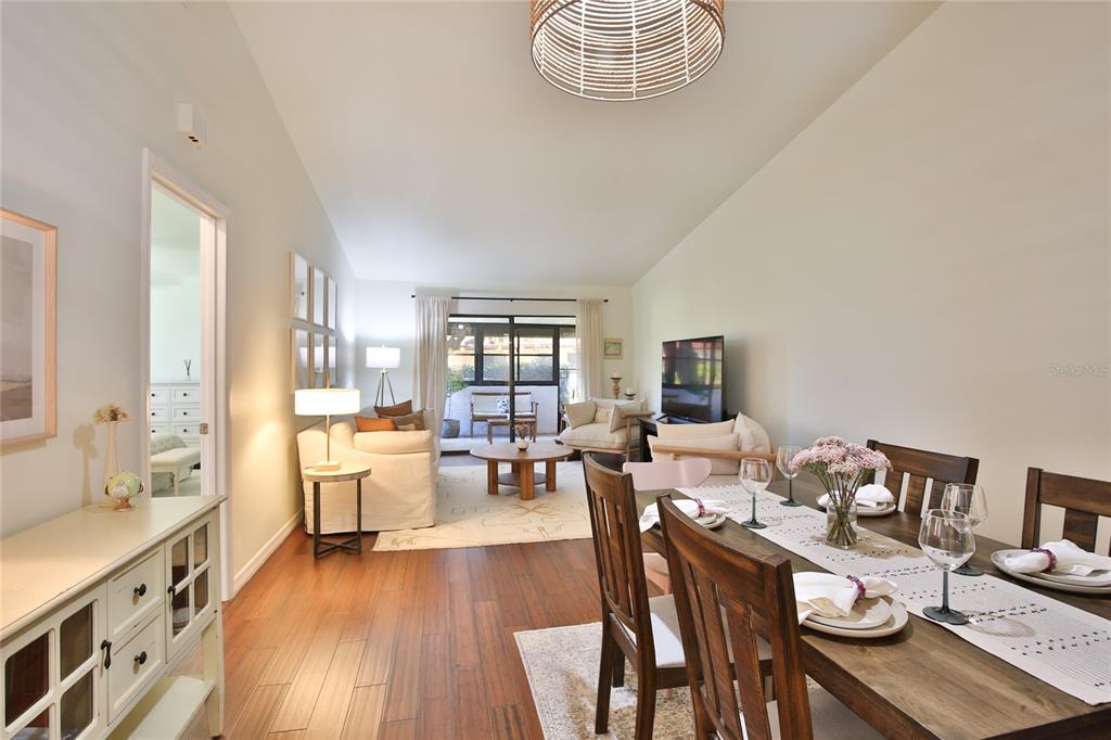 An open-concept living and dining area features wood flooring, a neutral color palette, and patio access — 1411 57TH STREET W UNIT 1411, BRADENTON, FL
