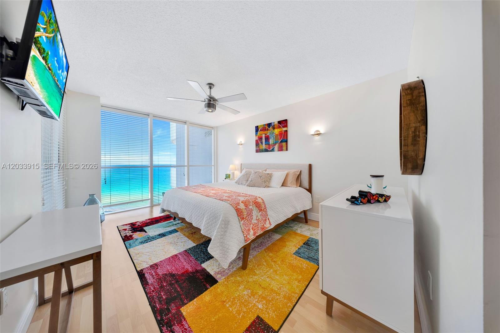 A bedroom features a bed, a colorful rug, a white dresser, and an ocean view — 6301 Collins Ave # 1708, Miami Beach FL 33141, MIAMI BEACH, FL