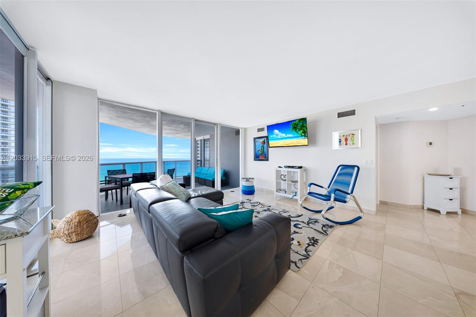 A living room with a dark leather sofa, blue rocking chair, and ocean view balcony — 6301 Collins Ave # 1708, Miami Beach FL 33141, MIAMI BEACH, FL