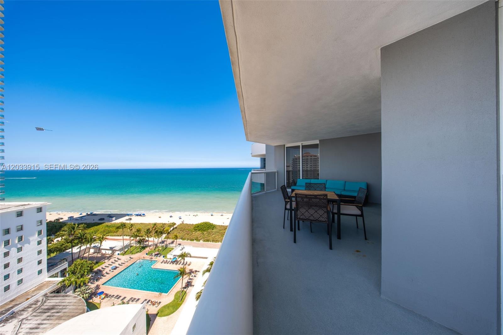 A high-rise balcony overlooks a beach, ocean, and swimming pool with outdoor dining furniture — 6301 Collins Ave # 1708, Miami Beach FL 33141, MIAMI BEACH, FL