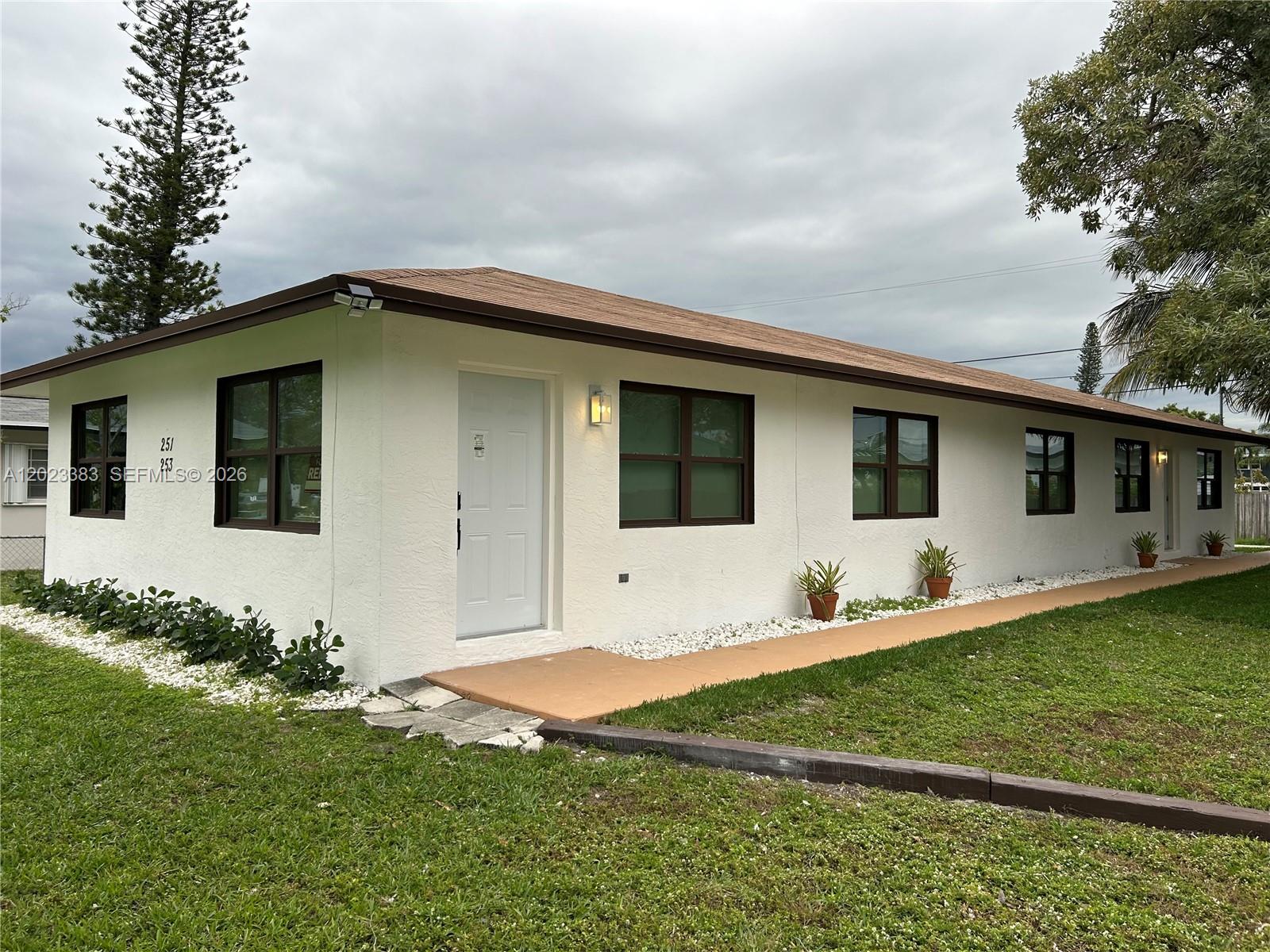 A single-story white house with a brown roof and dark-framed windows sits on a lawn — 251-253 SW 11th St, Dania Beach FL 33004, DANIA BEACH, FL