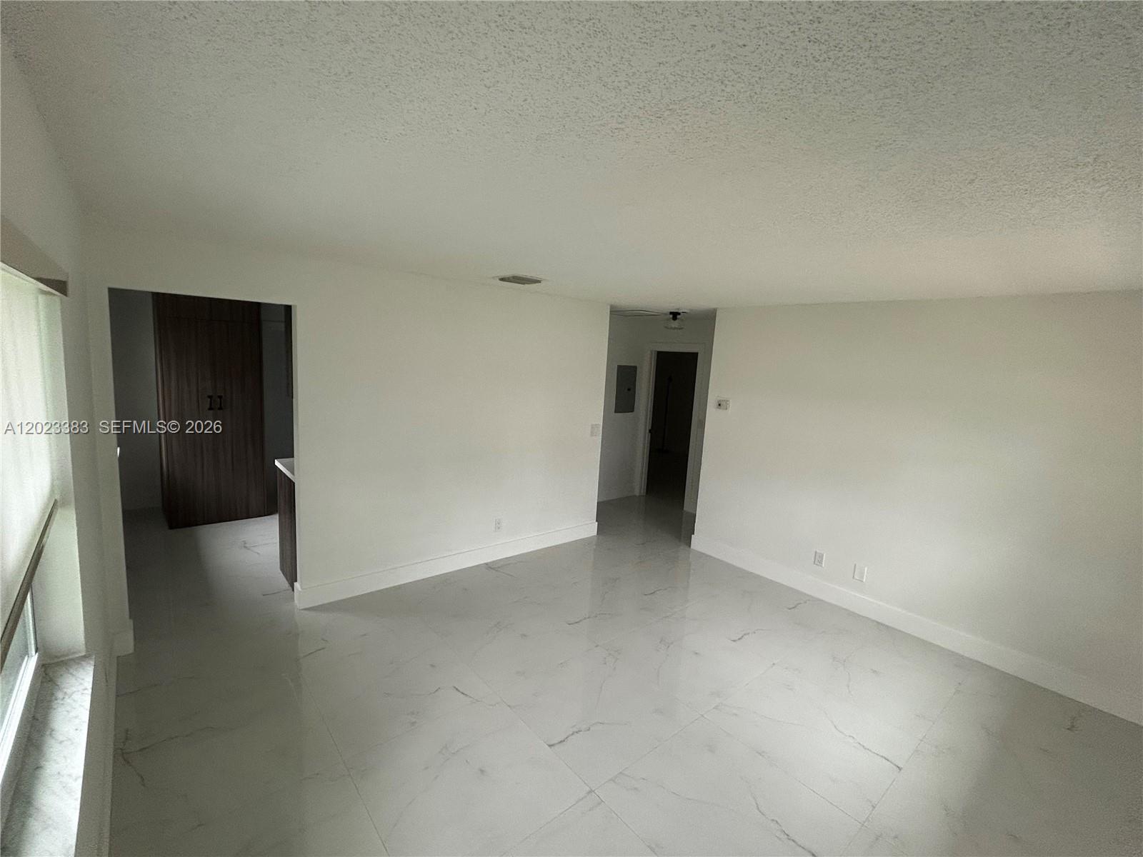 An empty room features white walls, a popcorn ceiling, and large white marble-look floor tiles — 251-253 SW 11th St, Dania Beach FL 33004, DANIA BEACH, FL