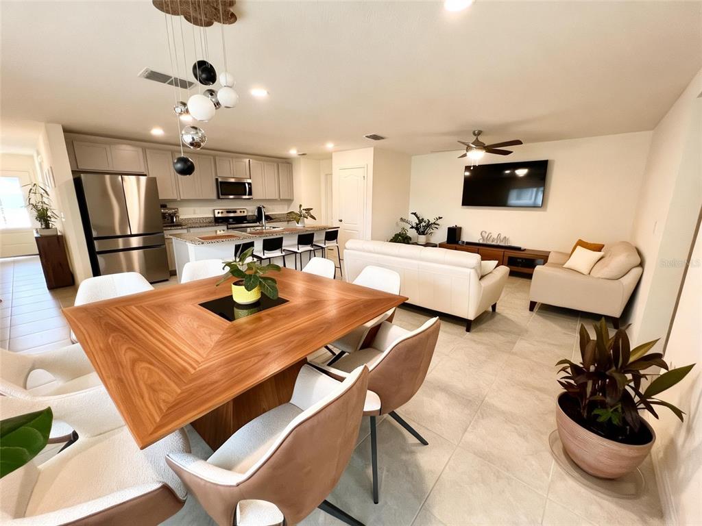 An open-concept living and dining area features a wooden table, white furniture, and kitchen island — 2727 MEADOW STREAM WAY, CLERMONT, FL