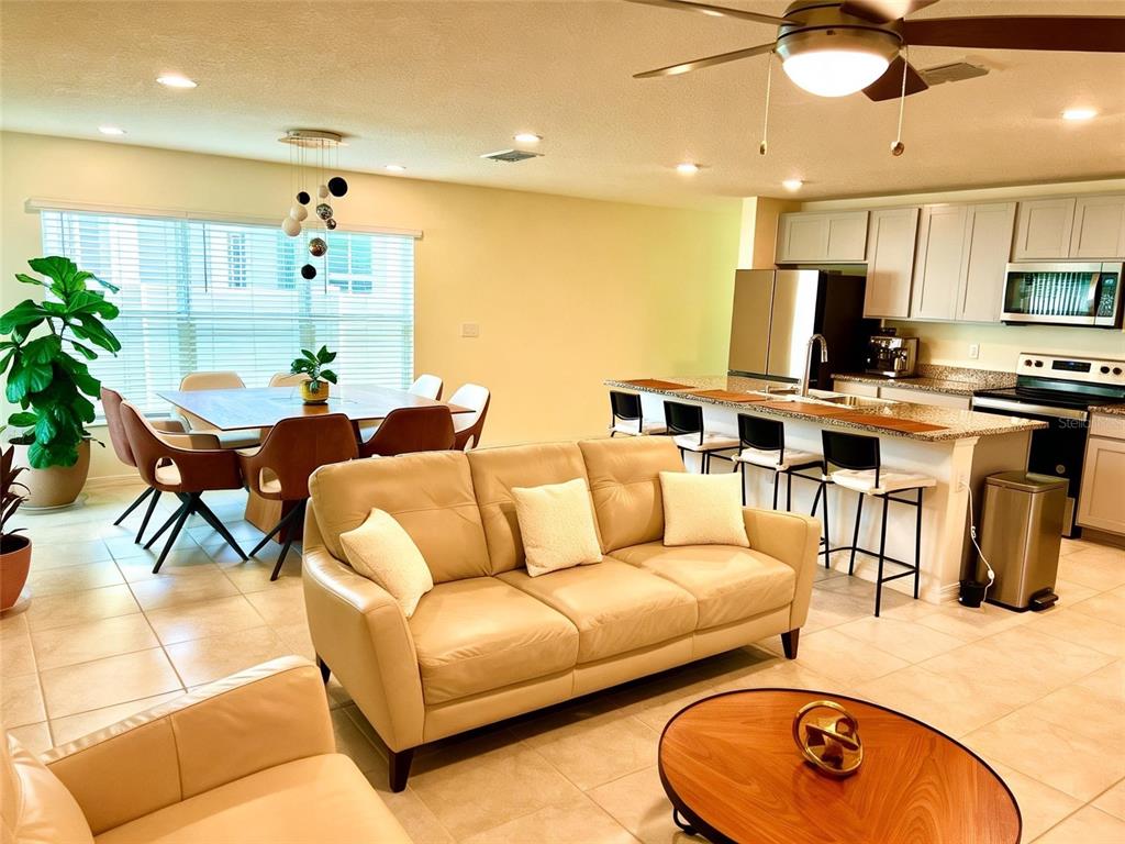 An open-concept living and dining area features a beige sofa, kitchen island, and tile flooring — 2727 MEADOW STREAM WAY, CLERMONT, FL