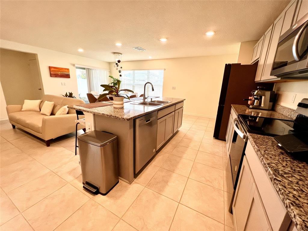 A kitchen with granite countertops and a central island overlooks a living room area — 2727 MEADOW STREAM WAY, CLERMONT, FL