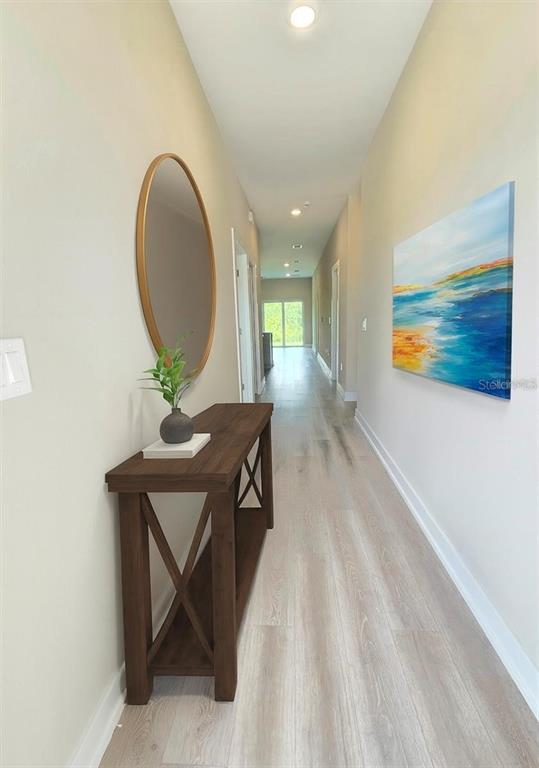 A long hallway features light wood-look flooring, a wooden console table, a mirror, and wall art — 12208-10 TETZEL AVENUE, PORT CHARLOTTE, FL