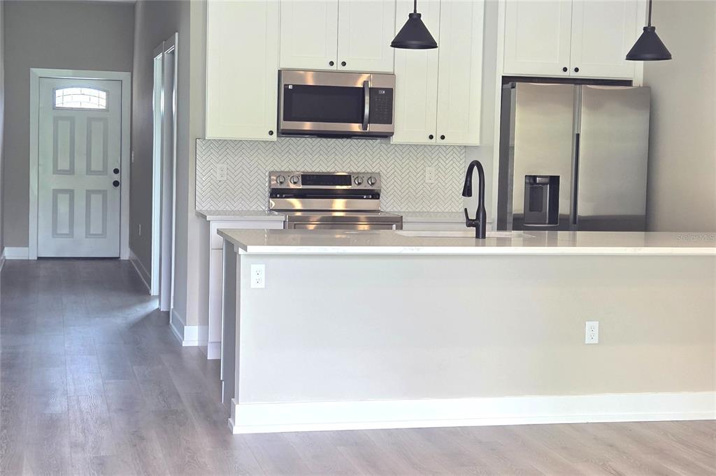 A kitchen features white cabinets, stainless steel appliances, a herringbone backsplash, and a breakfast bar — 12208-10 TETZEL AVENUE, PORT CHARLOTTE, FL
