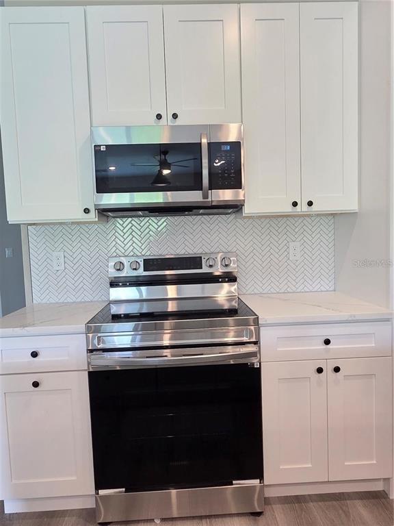 A kitchen features white shaker cabinets, stainless steel appliances, and a white herringbone tile backsplash — 12208-10 TETZEL AVENUE, PORT CHARLOTTE, FL
