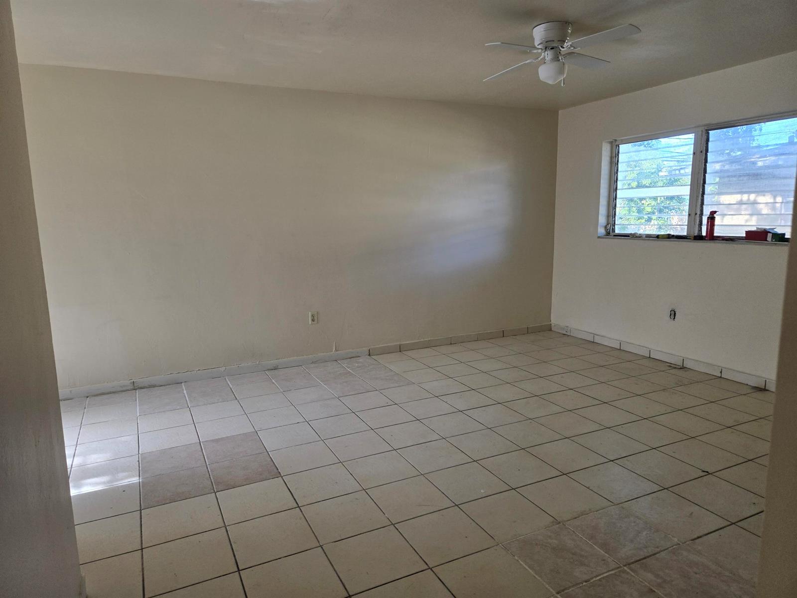 An empty room with beige walls, white tile flooring, a ceiling fan, and a window — 1560 NE 111th Street # 3, Miami FL 33161, MIAMI, FL