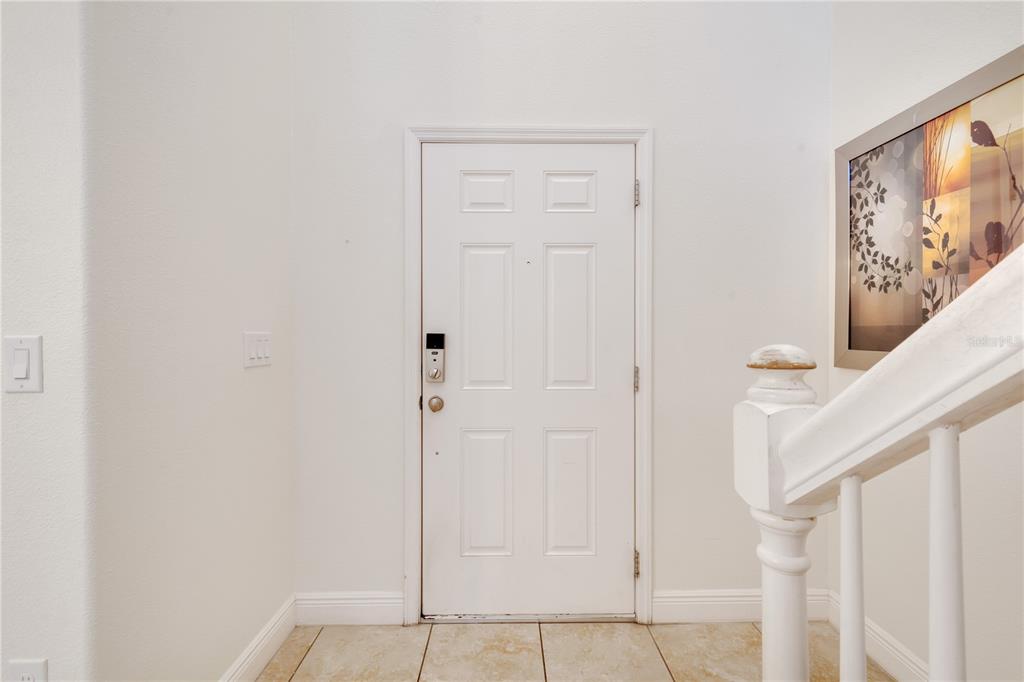 A white front door with a smart lock is situated in a tiled entryway — 4328 ACORN COURT, DAVENPORT, FL