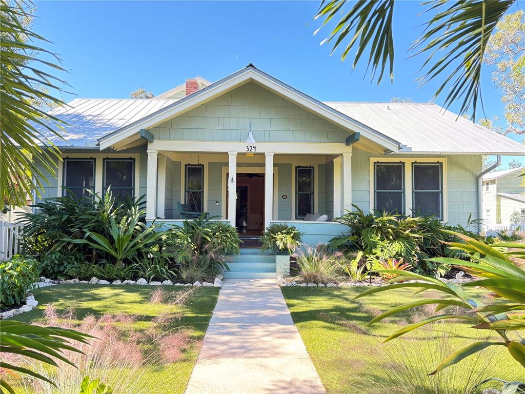 A light green bungalow features a covered front porch, metal roof, and lush landscaping — 324 JULIA PLACE, SARASOTA, FL