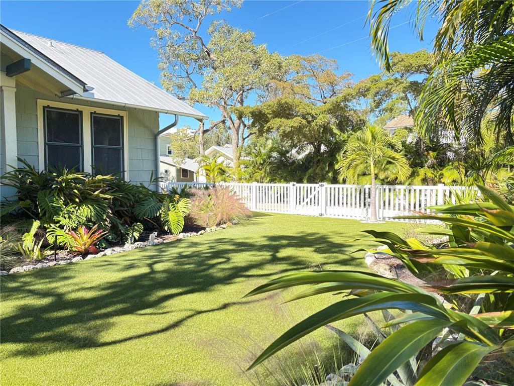 A green house with a metal roof overlooks a manicured lawn and white picket fence — 324 JULIA PLACE, SARASOTA, FL