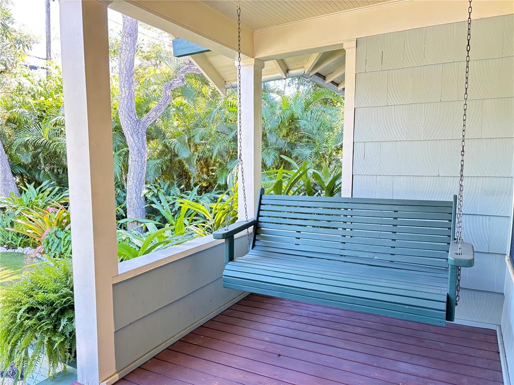 A green wooden porch swing hangs on a covered deck overlooking lush tropical landscaping — 324 JULIA PLACE, SARASOTA, FL