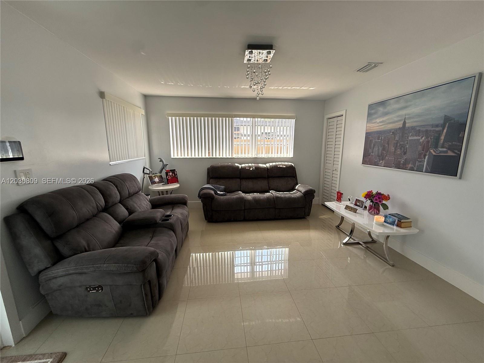 A living room features two dark gray reclining sofas, a white console table, and tile flooring — 10030 SW 213th Ter, Cutler Bay FL 33189, CUTLER BAY, FL