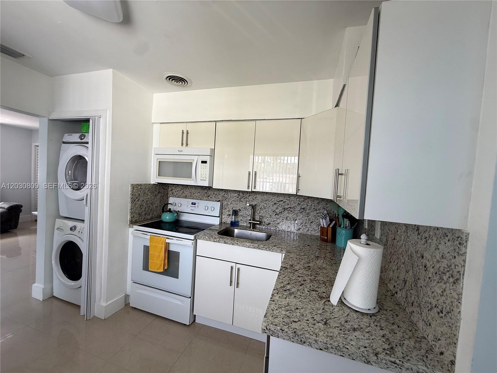 A kitchen features white cabinets, granite countertops, a stainless steel sink, and a stacked laundry unit — 10030 SW 213th Ter, Cutler Bay FL 33189, CUTLER BAY, FL