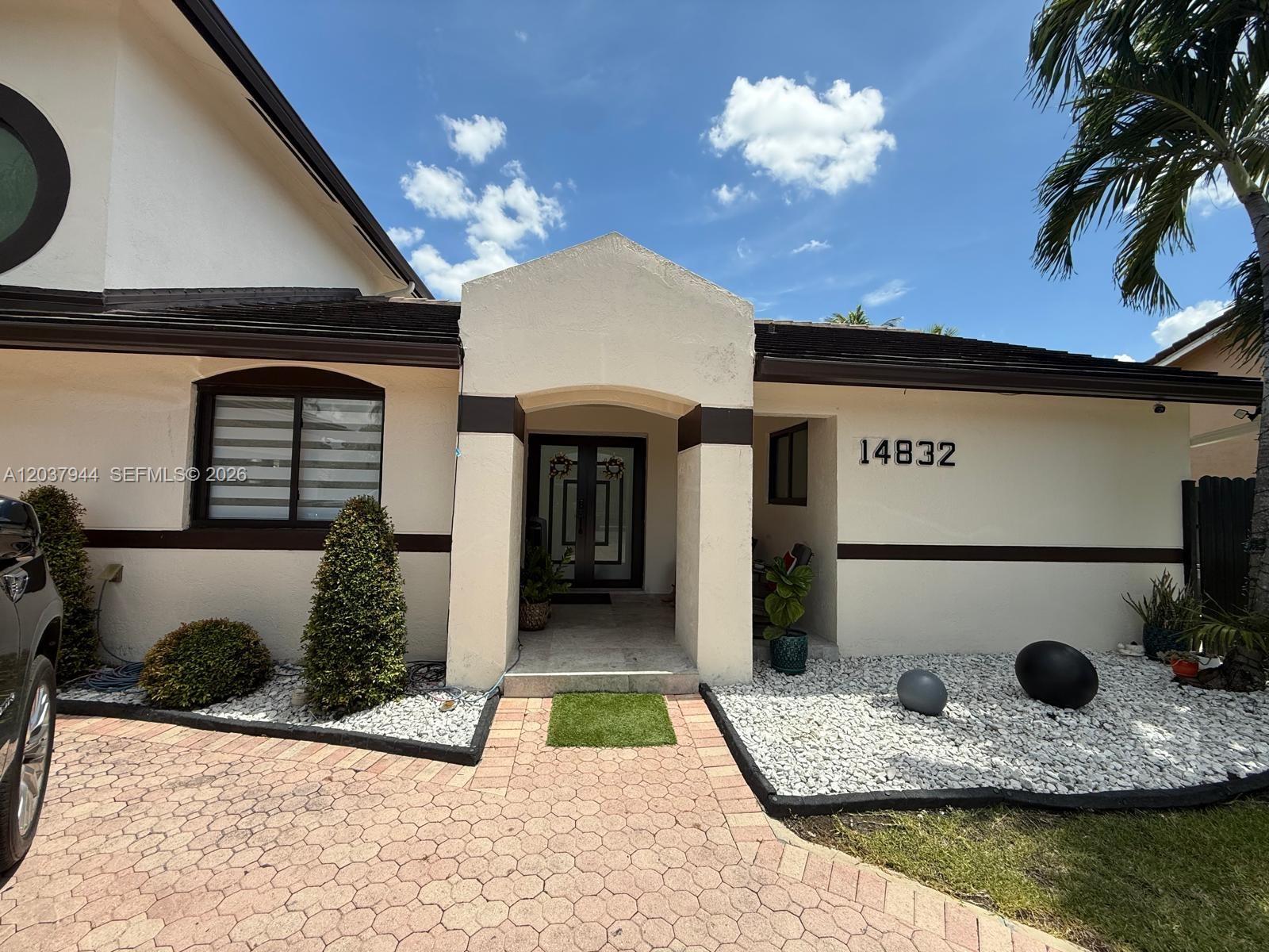 The exterior of a house features a paved driveway, a covered entryway, and white landscaping rocks — 14832 SW 169th Ln, Miami FL 33187, MIAMI, FL