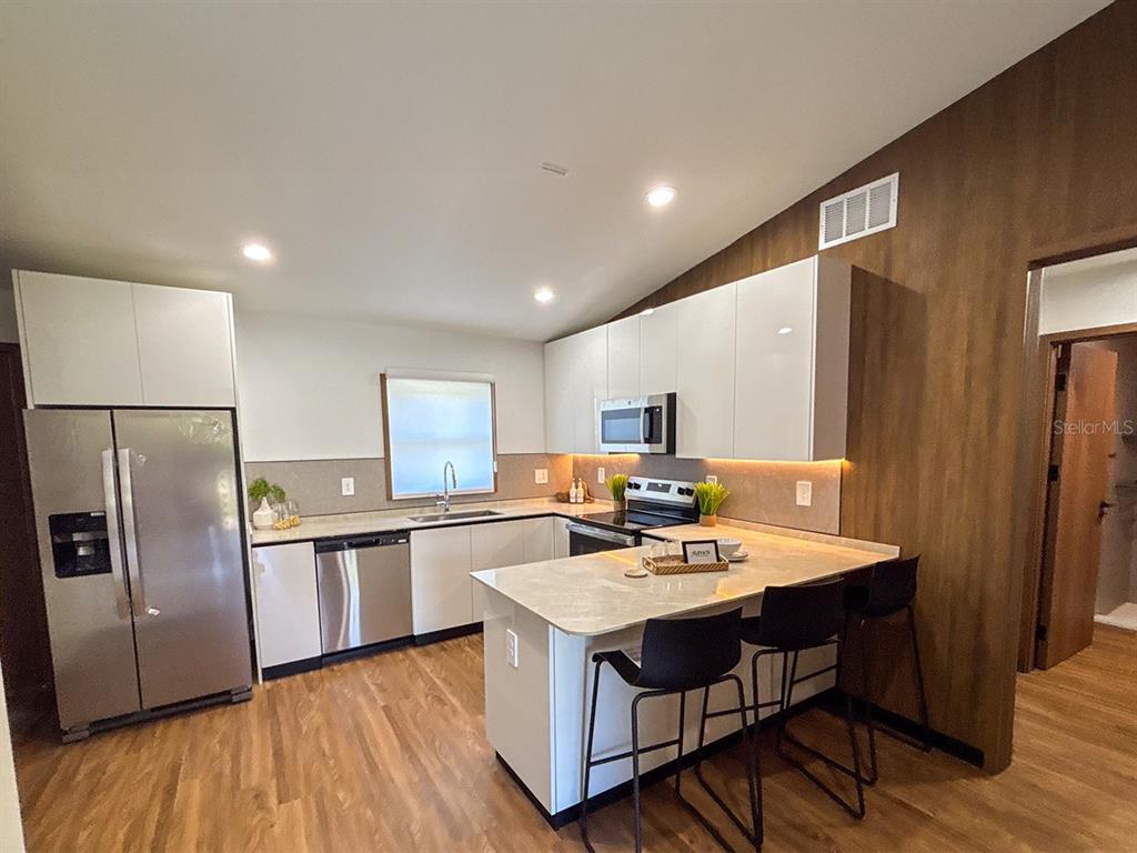A modern kitchen features white cabinets, stainless steel appliances, a breakfast bar, and wood flooring — 5830 VIRTUDES STREET, SEBRING, FL